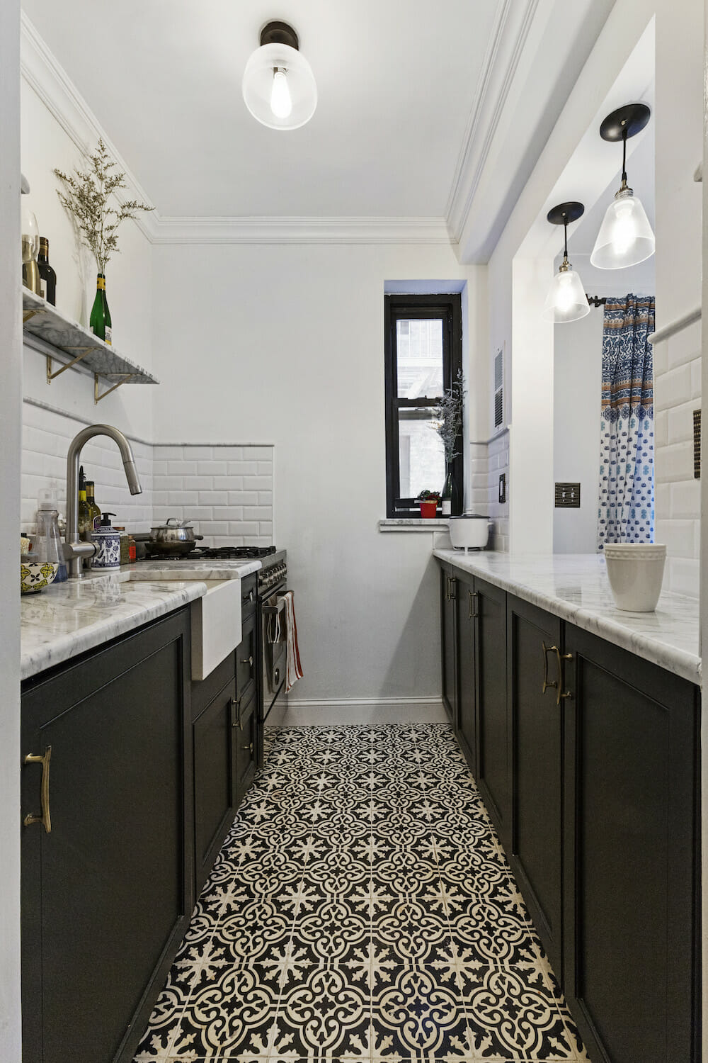 Galley kitchen with dark lower cabinets, marble counters, apron-front sink, subway tile, open marble shelf, and black-and-white tile floor.