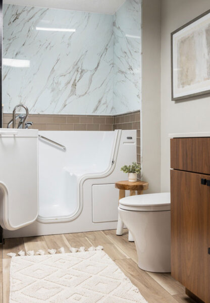 Elegant bathroom with a white walk-in tub, marble-style wall surround, wood vanity, and light wood flooring for an accessible, modern design.